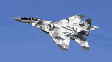 a camouflaged fighter jet is flying through a blue sky .