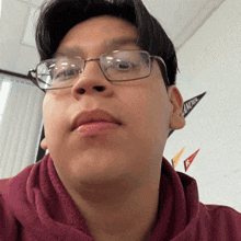 a young man wearing glasses and a maroon sweatshirt looks at the camera with a banner in the background that says front