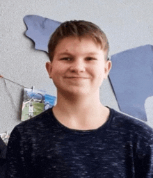 a young boy wearing a blue sweater is smiling in front of a wall with a picture of a man on it .