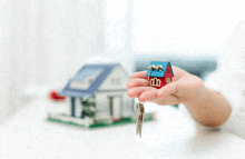 a person is holding a small model house and keys