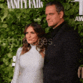 a man and a woman are posing for a picture in front of a wall with vanity fair written on it