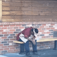 a man sits on a bench in front of a brick wall that says ' a ' on it