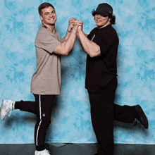 two men are holding hands in front of a blue backdrop