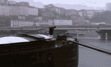 a man stands on the deck of a boat with a bridge in the background and a building that says ford on it