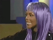 the woman is wearing a purple wig and smiling .