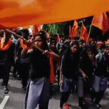 a group of people are marching down a street holding flags and a woman is holding an orange flag .