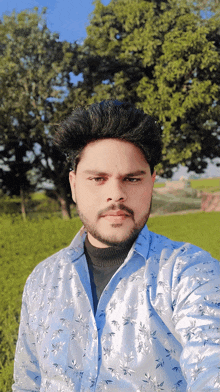 a man in a floral shirt takes a selfie in a field