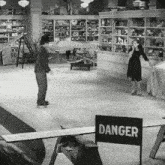 a black and white photo of a man and a woman in a store with a sign that says danger