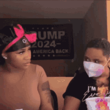 two women wearing face masks in front of a trump sign