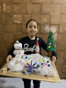 a little girl wearing a barbie sweater is holding a christmas display