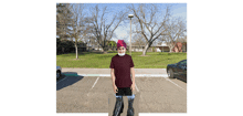 a man wearing a red hat and sunglasses is standing in a parking lot with trees in the background