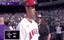 a baseball player wearing a red hat and a white jersey with the word angel on it is standing in front of a crowd .