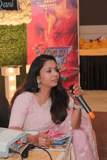 a woman in a pink saree is holding a microphone in front of a sign that says rani