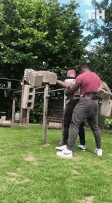 two men are standing in a grassy field fighting each other . one of the men is wearing a red shirt .