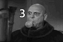 a black and white photo of a bald man blowing a bubble with the number three in the background .