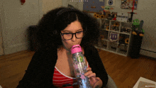 a woman wearing glasses and headphones is drinking from a pink bottle that says shagarita on the top