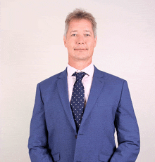 a man in a blue suit and polka dot tie stands with his hands in his pockets