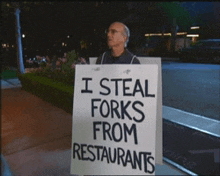 a man is holding up a sign that says i steal forks from restaurants