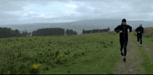 a couple of people running in a field with a building in the background