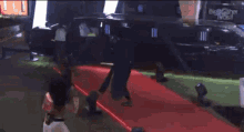 a woman walking on a red carpet in front of a black car that says big brother