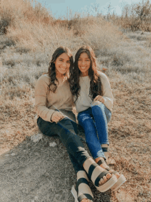 two girls are sitting next to each other on a grassy hillside