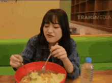 a woman is sitting at a table with a bowl of food and a bottle of water in front of a transmedia sign