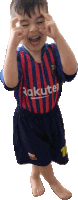 a young boy wearing a rakuten shirt and shorts makes a funny face