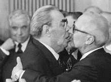 a man in glasses kisses another man in a suit