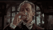 a man in a suit and bow tie drinks from a glass