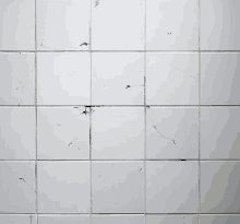 a white tile wall with a few cracks and stains