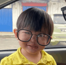 a young boy wearing glasses and a yellow shirt is sitting in a car and smiling .