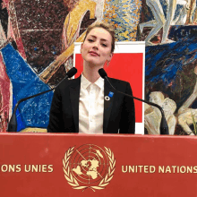 a woman stands at a podium with united nations written on it