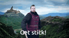 a man in a red vest stands in front of a mountain with the words get stick written on the bottom