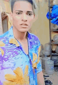 a young man in a blue and purple shirt is standing in front of a shelf with water bottles on it