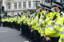 a large group of police officers wearing face masks are standing in a line on the side of a street .