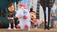 a stuffed unicorn with a pink horn is standing in front of a group of children .