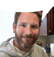 a man with a beard and ear piercings is smiling in a kitchen