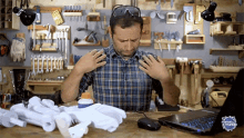 a man in a plaid shirt is sitting at a table with a laptop and a bottle of glue in front of him