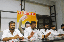 a group of men sit at a table in front of a jai congress sign