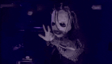 a person wearing a mask and dreadlocks is standing on a stage in front of a purple background .