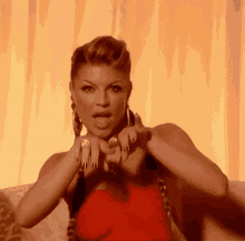 a woman in a red dress is making a heart shape with her hands and sticking her tongue out .