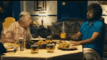 two men are sitting at a table with plates of food and glasses of whiskey .