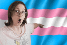 a woman wearing glasses and a t-shirt with a drawing of a pencil on it points to a transgender flag