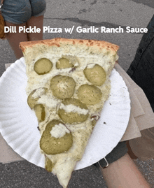 a slice of dill pickle pizza w / garlic ranch sauce is on a paper plate