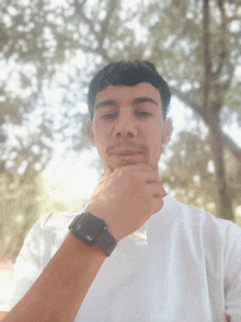 a man wearing a white shirt and a black watch has his hand under his chin