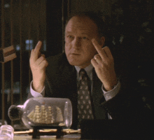 a man in a suit and tie is sitting at a desk giving the middle finger