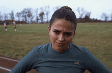 a woman is standing in a field with her hands on her hips and making a funny face .