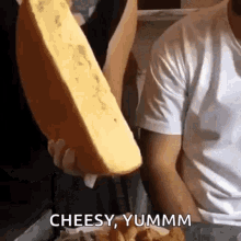 a man is holding a large piece of cheese and saying `` cheesy yummm '' .