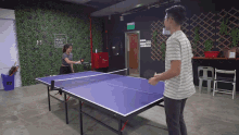 a man and a woman are playing ping pong in a room with a sign that says what 's your goal