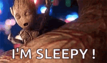 groot is sleeping on a bed with the words `` i 'm sleepy '' written next to him .